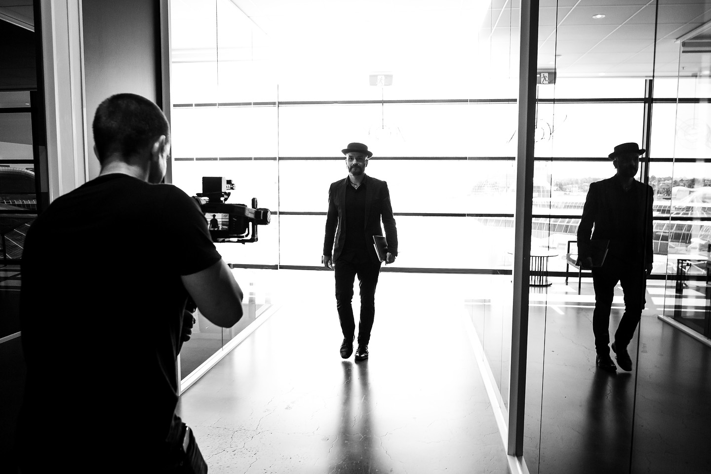 Behind-the-scenes silhouette of Arek being filmed walking through a glass corridor